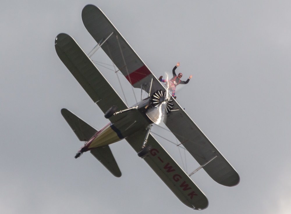 Person standing on top of a plane while it is flying overhead.